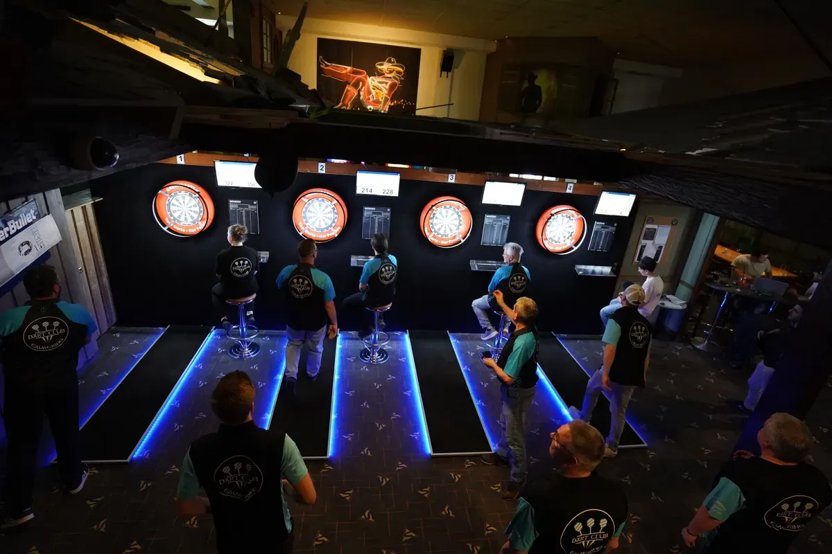 Spielerinnen und Spieler in Vereinsshirts an den Dartboards beim Abschlussturnier